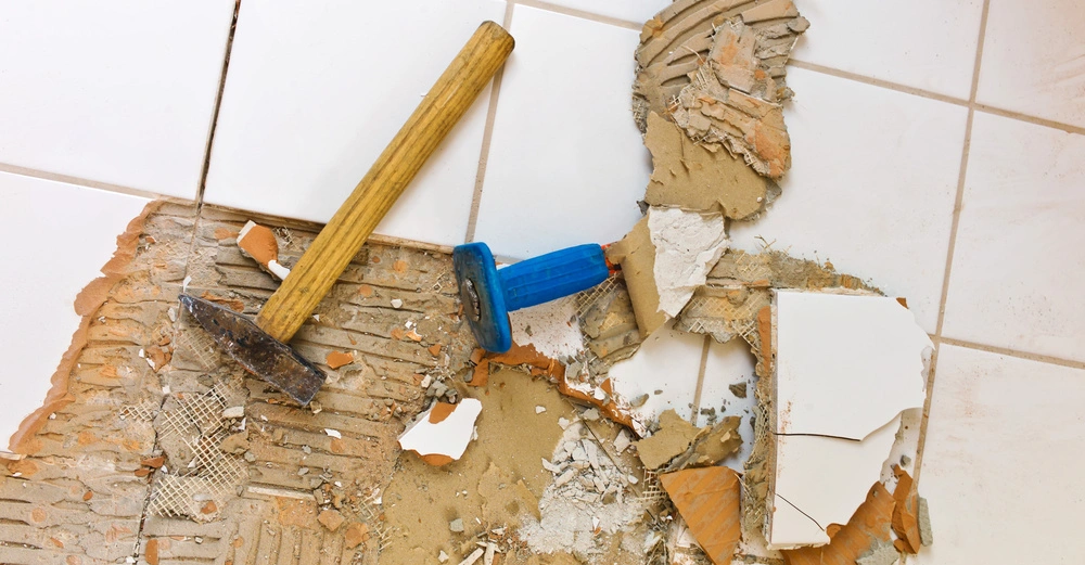 Hammer und Meißel zerschlagen Fliesen auf einem weißen gefliesten Boden in einer Baustellenumgebung.