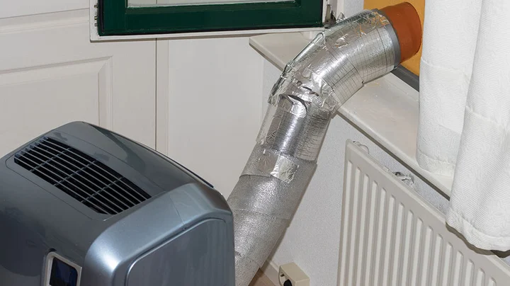 Eine mobile Klimaanlage, die vor einem abgedeckten Fenster steht. Der Abluftschlauch wurde mit einer zusätzlichen Isolierung abgedichtet, damit keine Hitze in den Raum entkommen kann.