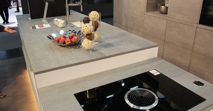 Galerie-Bild 14: Moderne Küche zeigt eine Arbeitsplatte mit integrierter Spüle und Induktionskochfeld verziert mit einer Schale voller Äpfel und zwei hohen Glasvasen mit dekorativen Kugeln aus Holz und Garn.