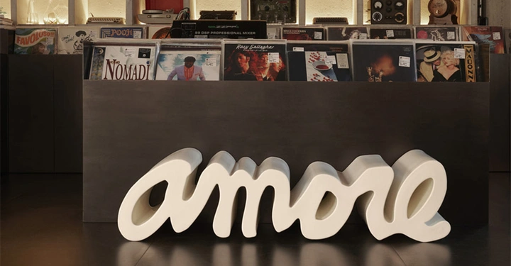 hellbeige AMORE Sitzbank aufgestellt vor einem Restauranttresen. Der Raum in dunklem Braun gehalten, der Amore-Schriftzug sticht hervor