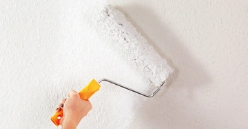 Eine Malerwalze mit weißer Farbe fährt über eine helle Wand.